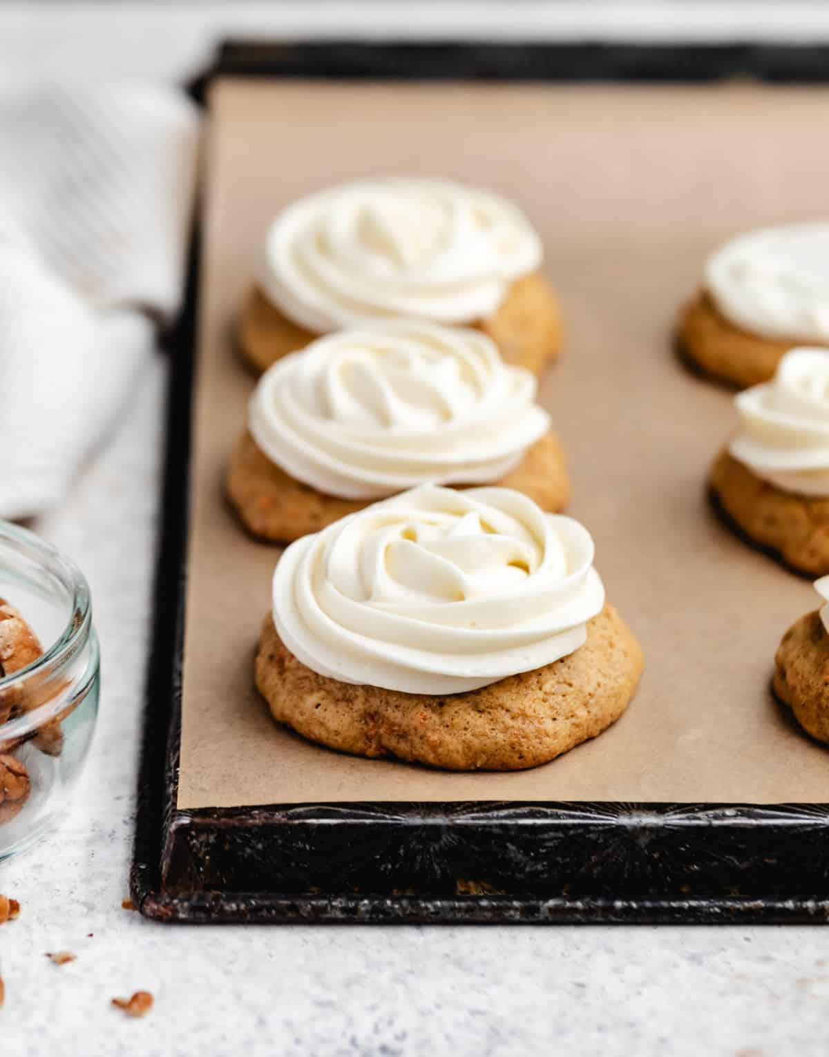 Frosted carrot cake cookies next to a dish of chopped pecans.