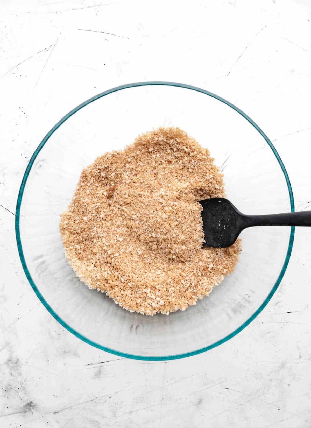 Breadcrumbs and spices stirred together in a glass mixing bowl. 