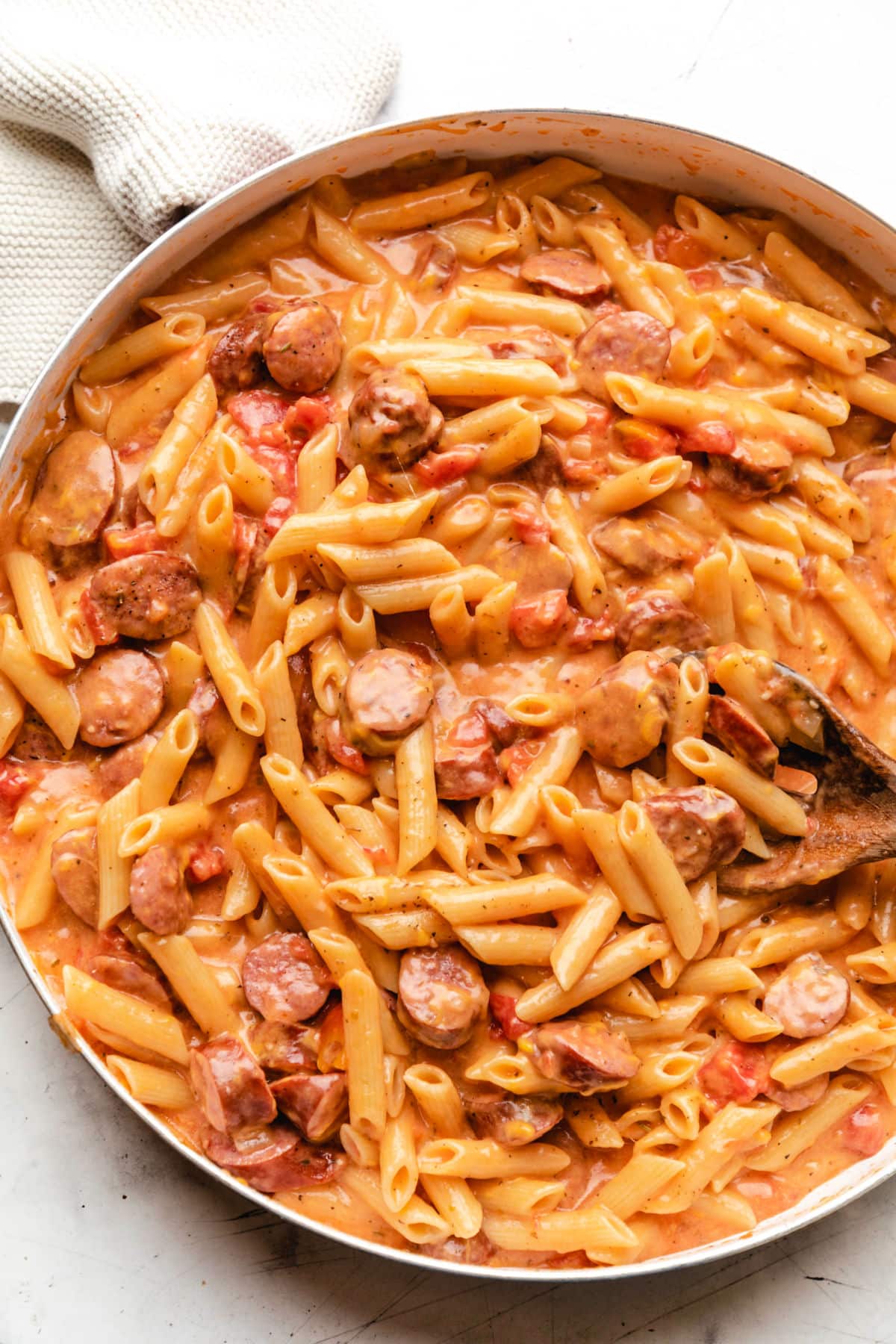 A wooden spoon in a skillet of cheesy kielbasa pasta.