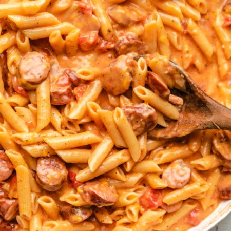 A wooden spoon scooping up cheesy kielbasa pasta.