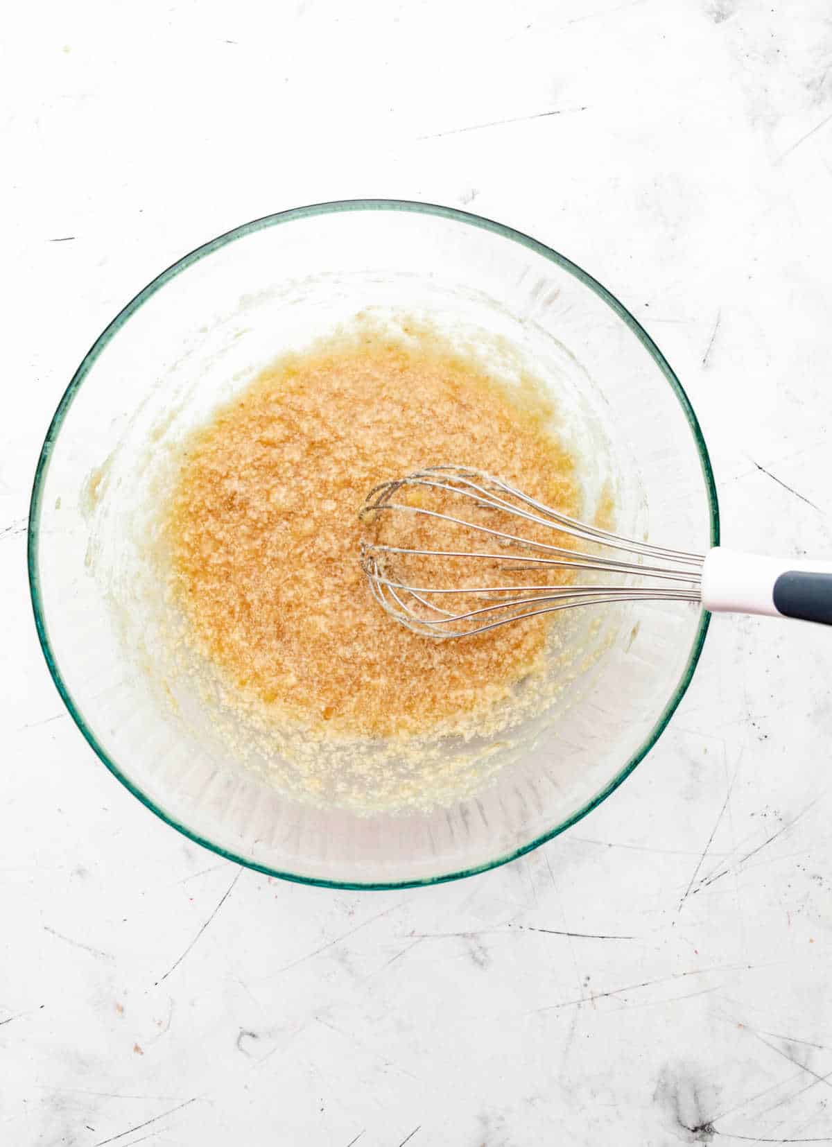 Sugars whisked into banana mixture in a glass mixing bowl. 