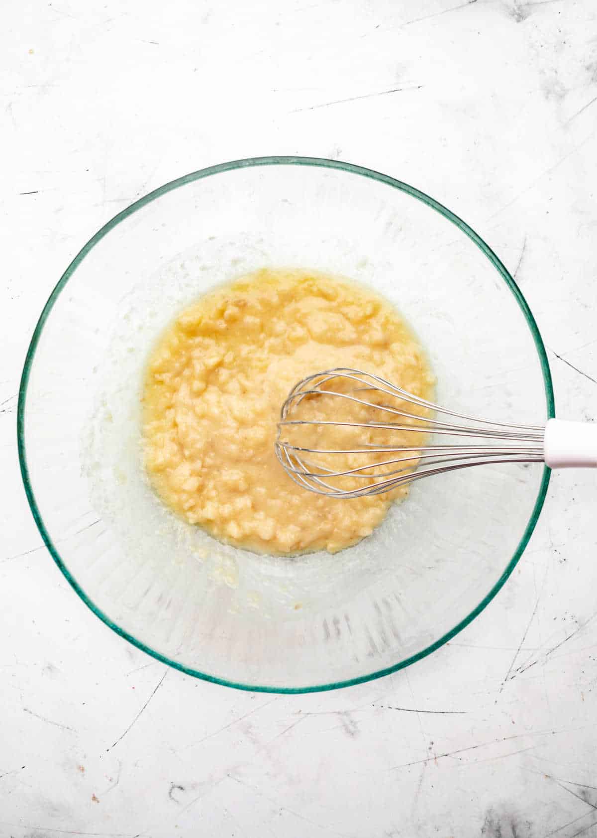 Mashed banana and melted butter mixed in a glass mixing bowl.