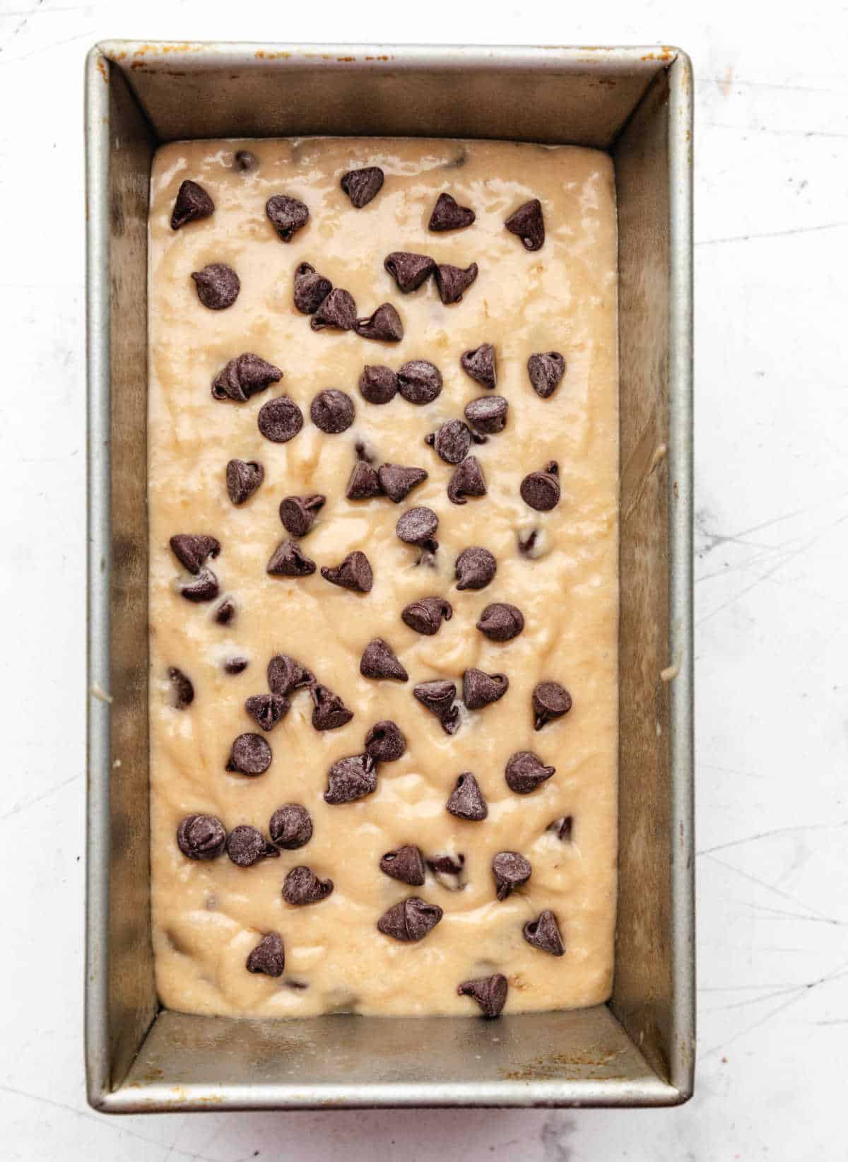 Chocolate chip banana bread batter topped with chocolate chips in a loaf pan.