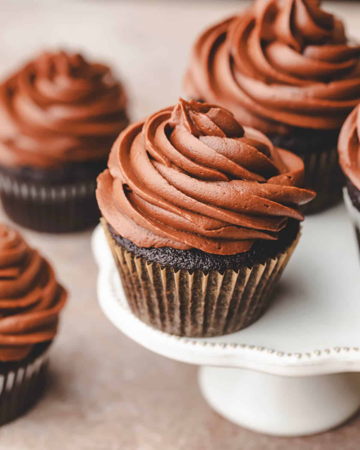 Chocolate cream cheese frosted chocolate cupcakes on a white cake stand.