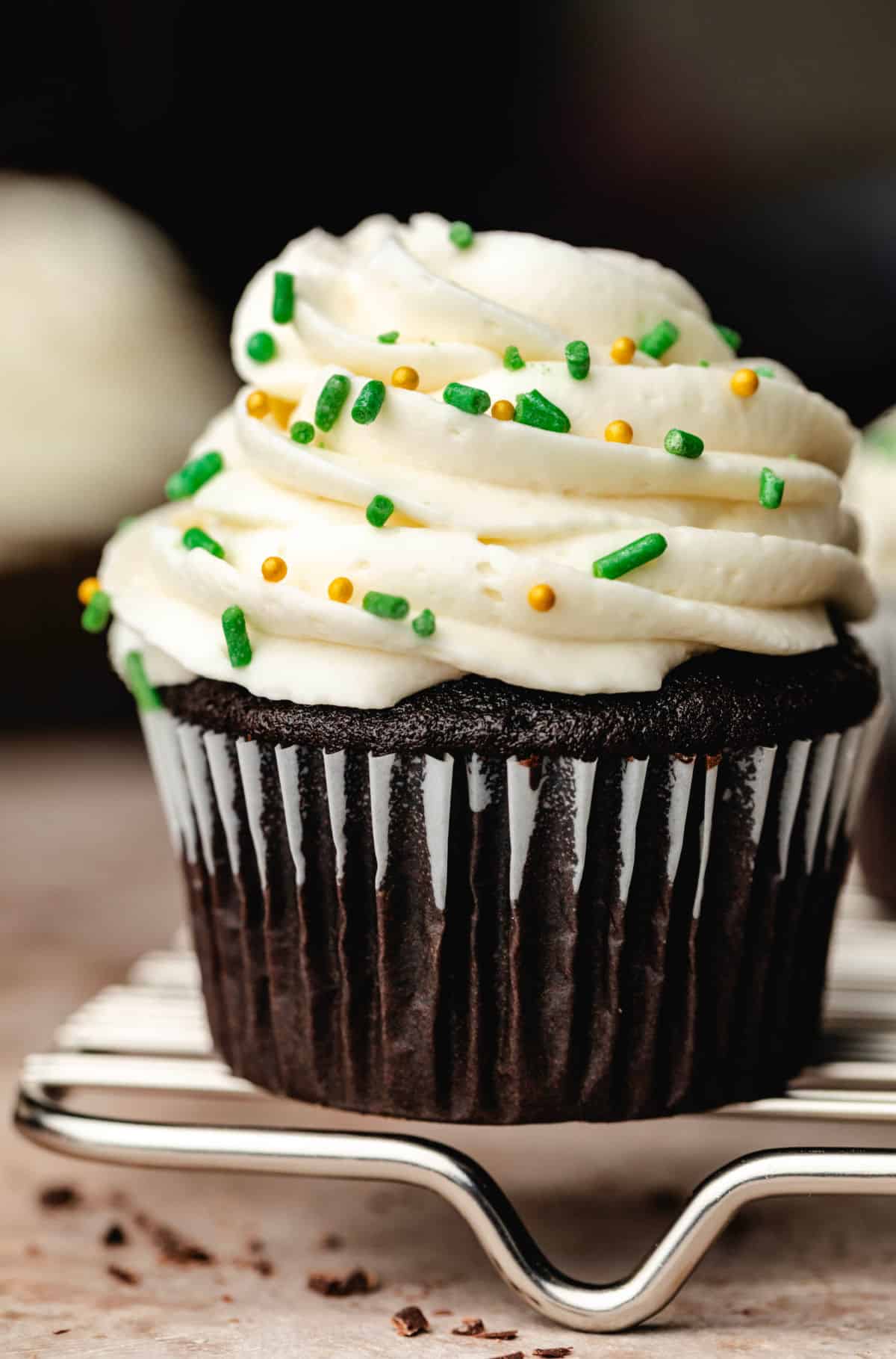 A Guinness cupcake topped with cream cheese frosting and green and gold sprinkles. 
