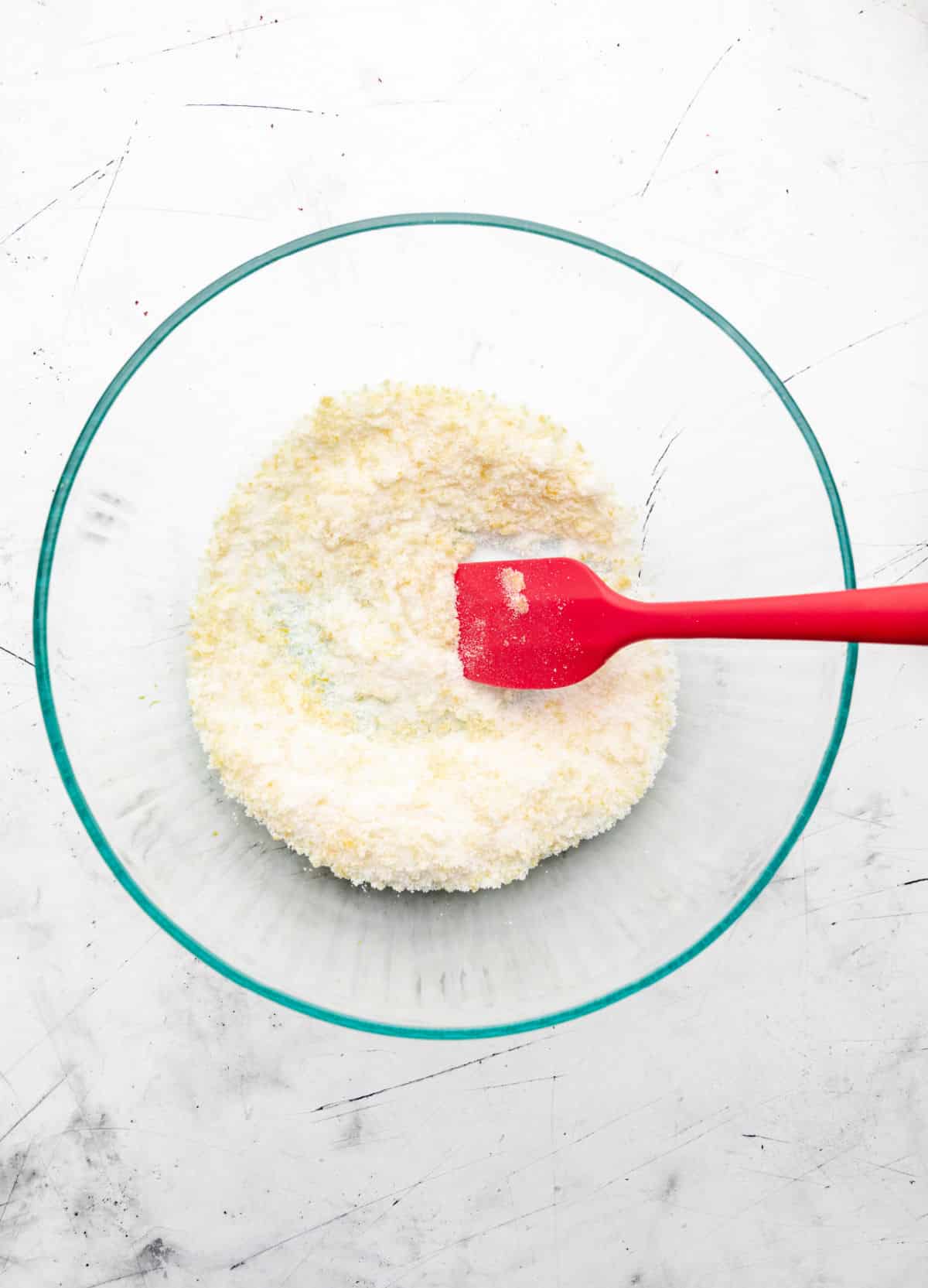 A red rubber spatula rubbing lemon zest into sugar. 