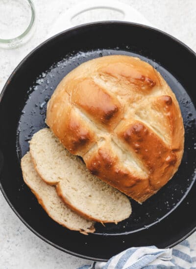 A loaf of skillet bread with two pieces sliced in a skillet.