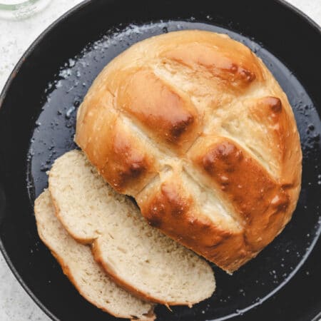 A loaf of skillet bread with two pieces sliced in a skillet.