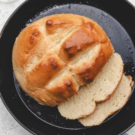 A loaf of skillet bread in a cast iron skillet with two slices next to it.