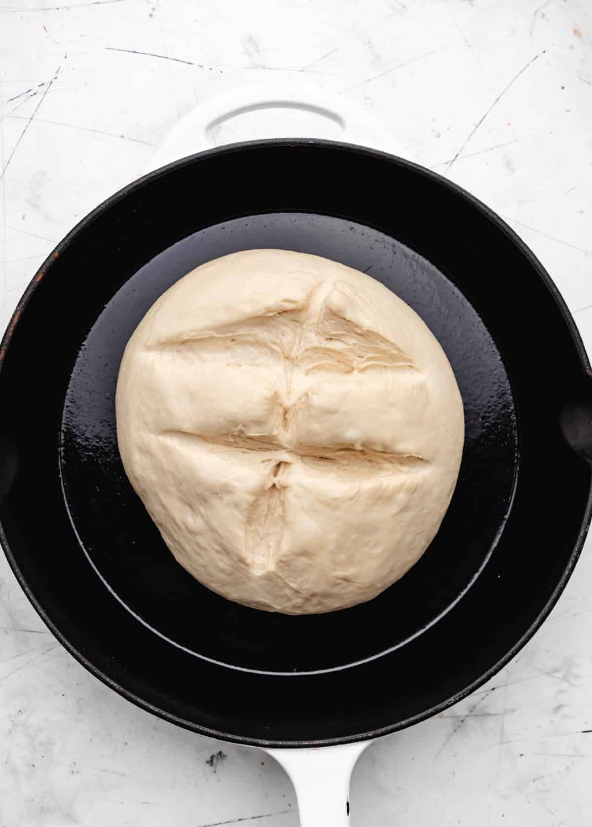 Skillet bread dough with slits cut into it. 