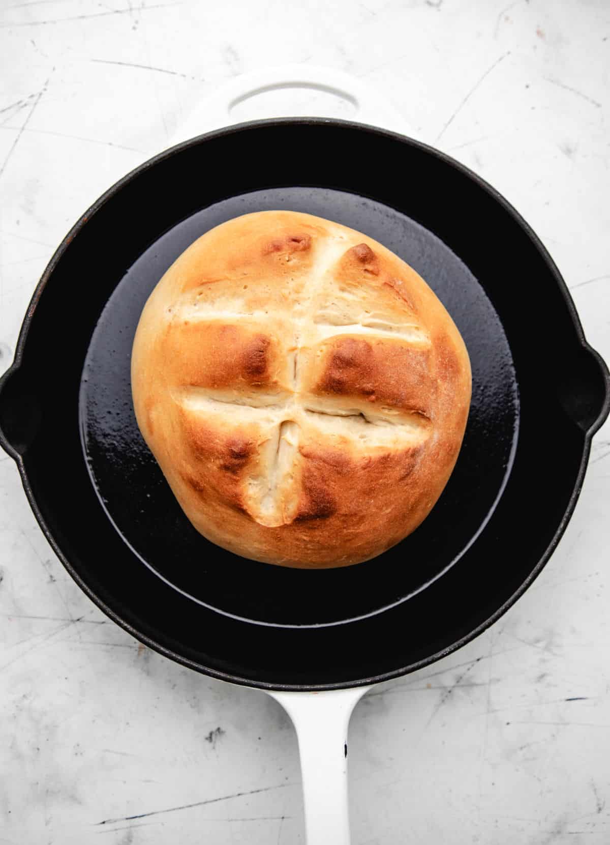 A loaf of baked skillet bread in a white enamel cast iron skillet.