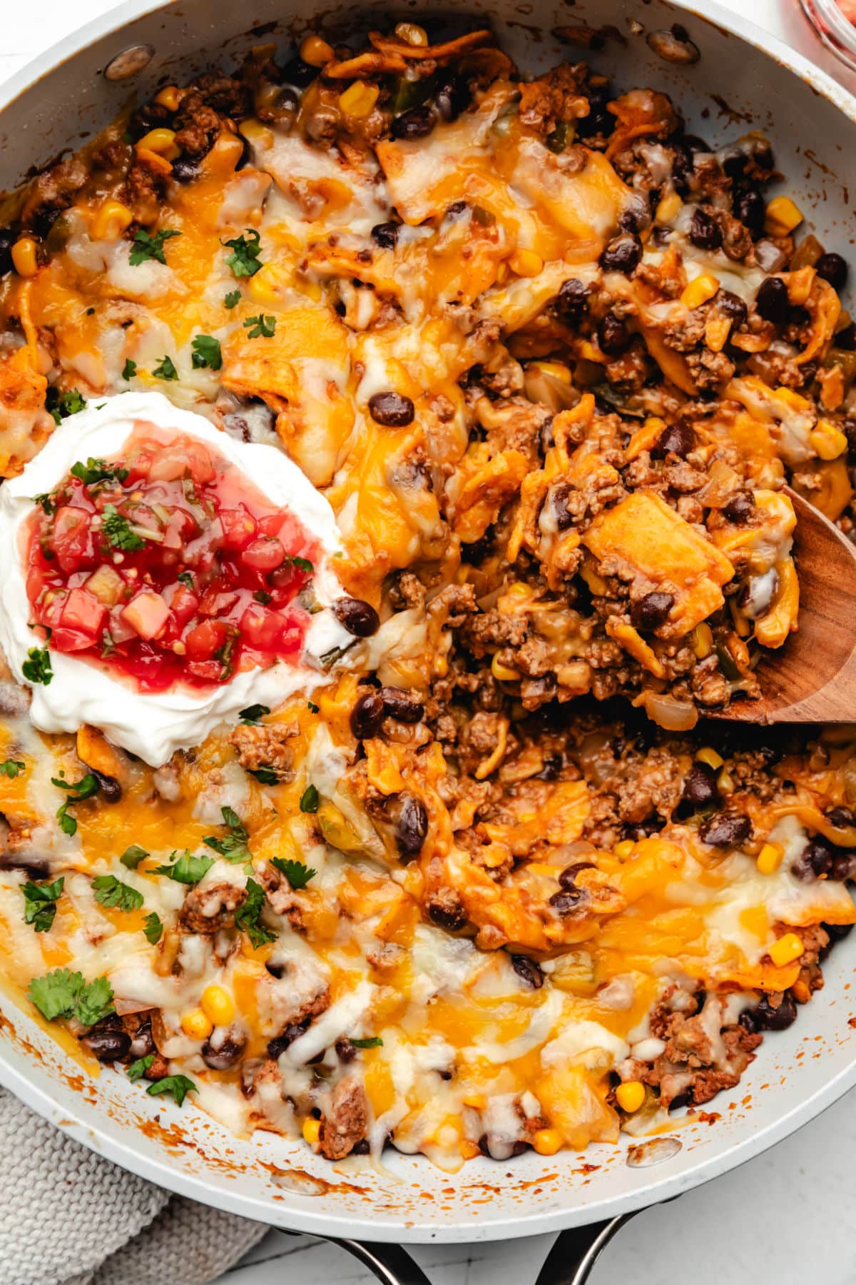 A wooden spoon in a pan of skillet enchiladas.