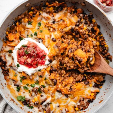 A wooden spoon holding a scoop of skillet enchiladas in a pan.