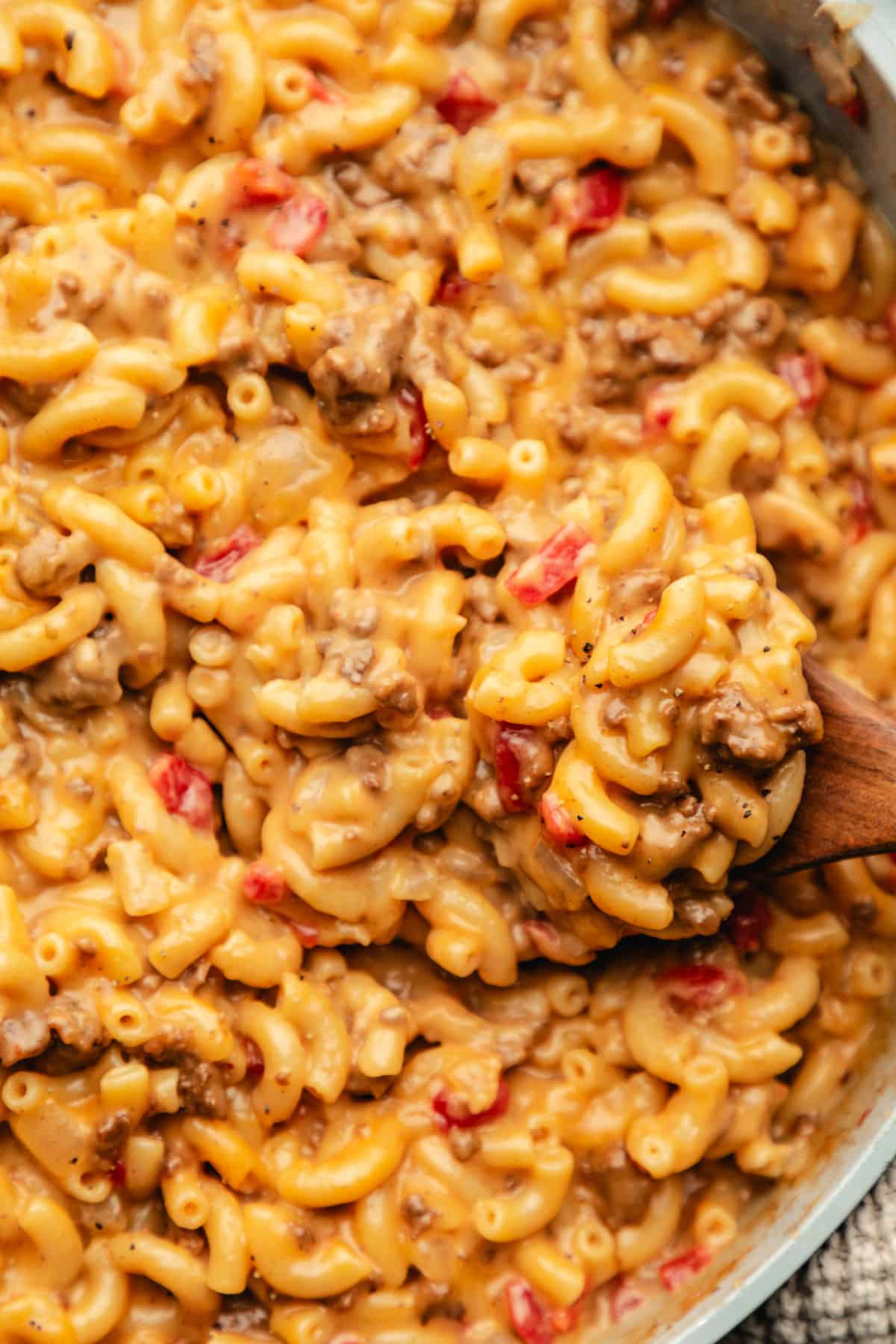A wooden spoon holding a scoop of cheeseburger macaroni over the skillet.