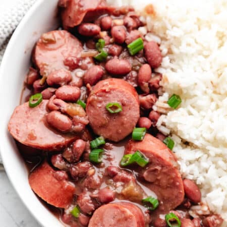 Slow cooker red beans and rice in a white dish topped with sliced green onion.
