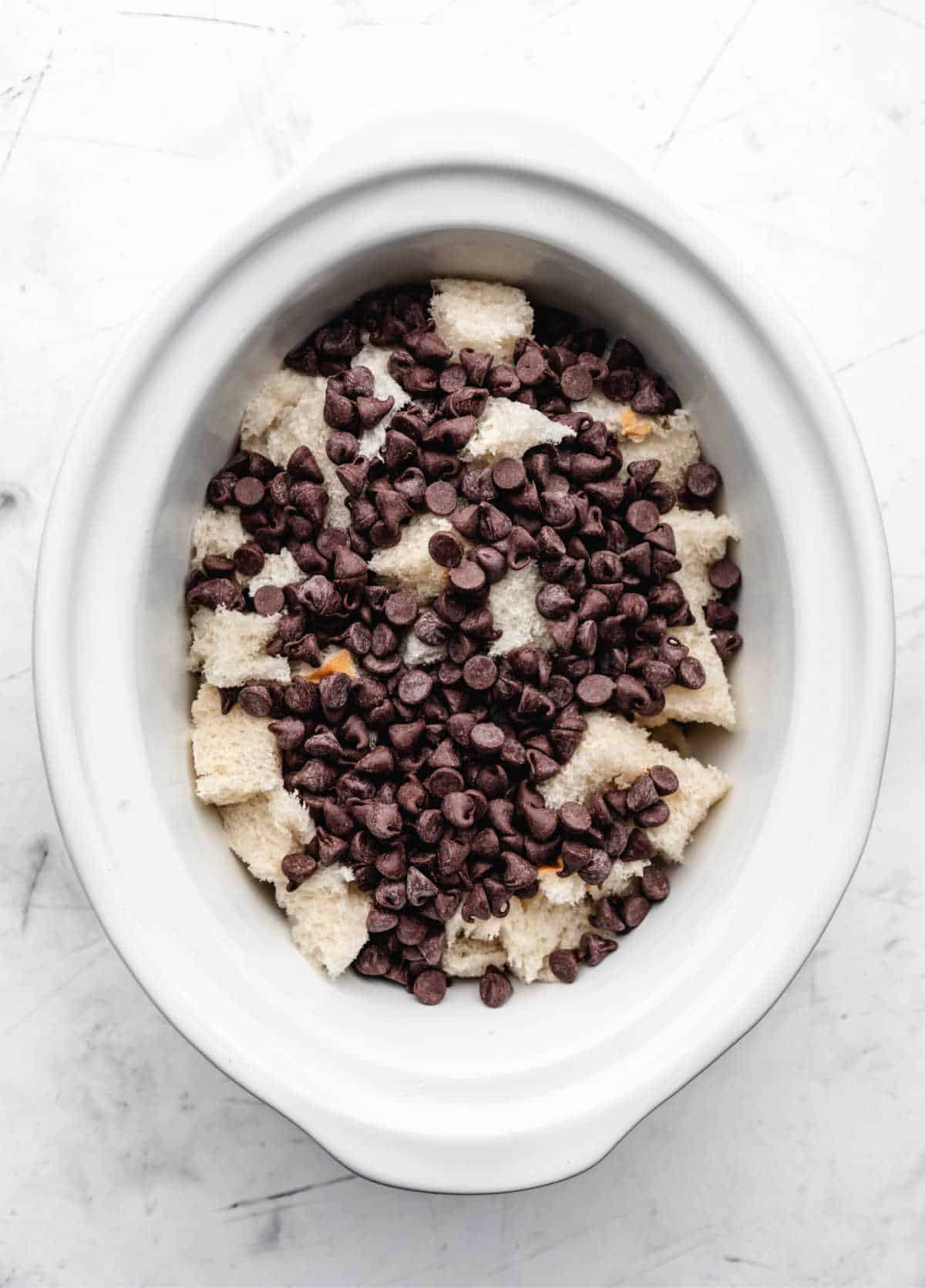 Chocolate chips on top of cubes of bread in a slow cooker.