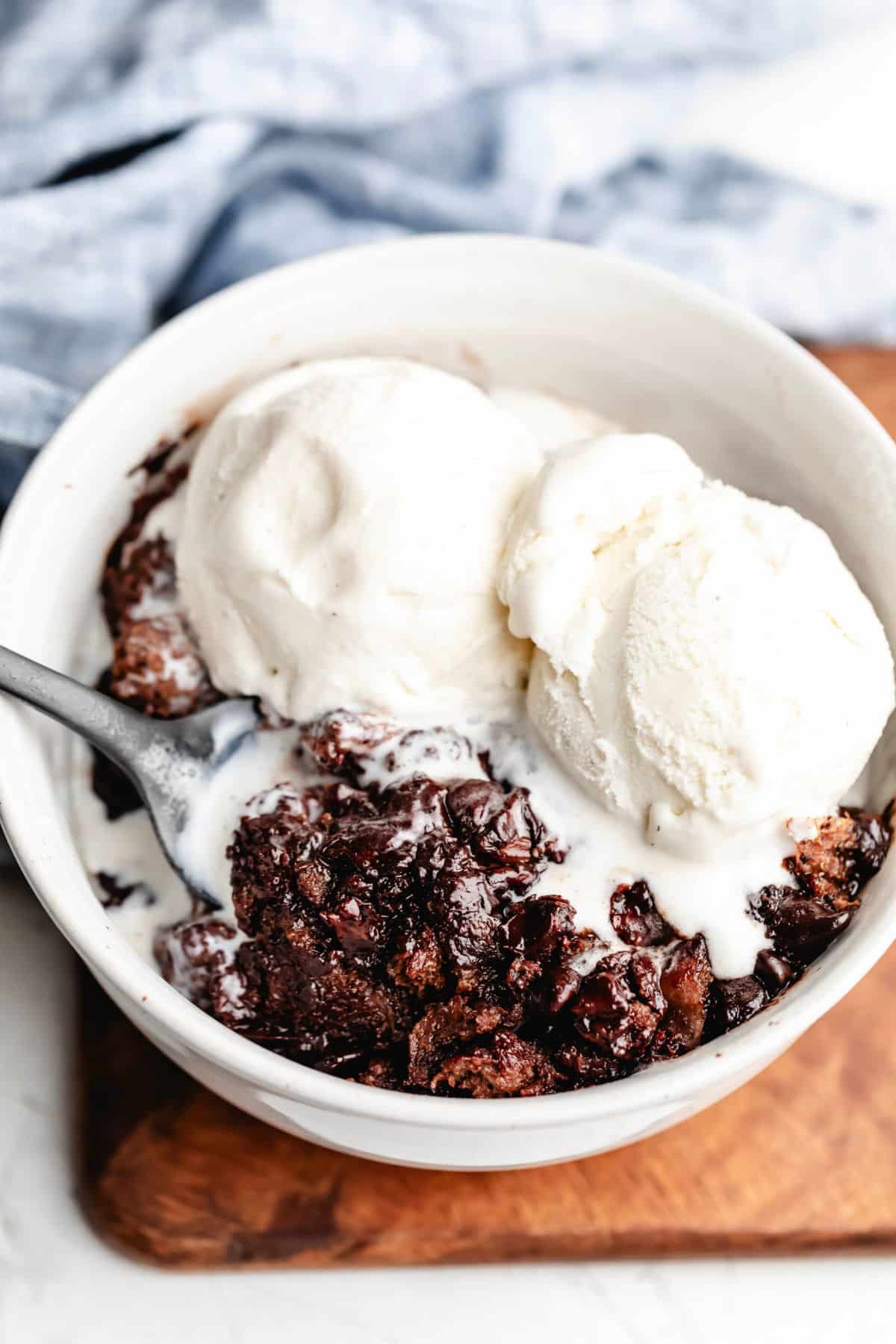 Crock pot triple chocolate bread pudding in a white dish topped with two scoops of vanilla ice cream.