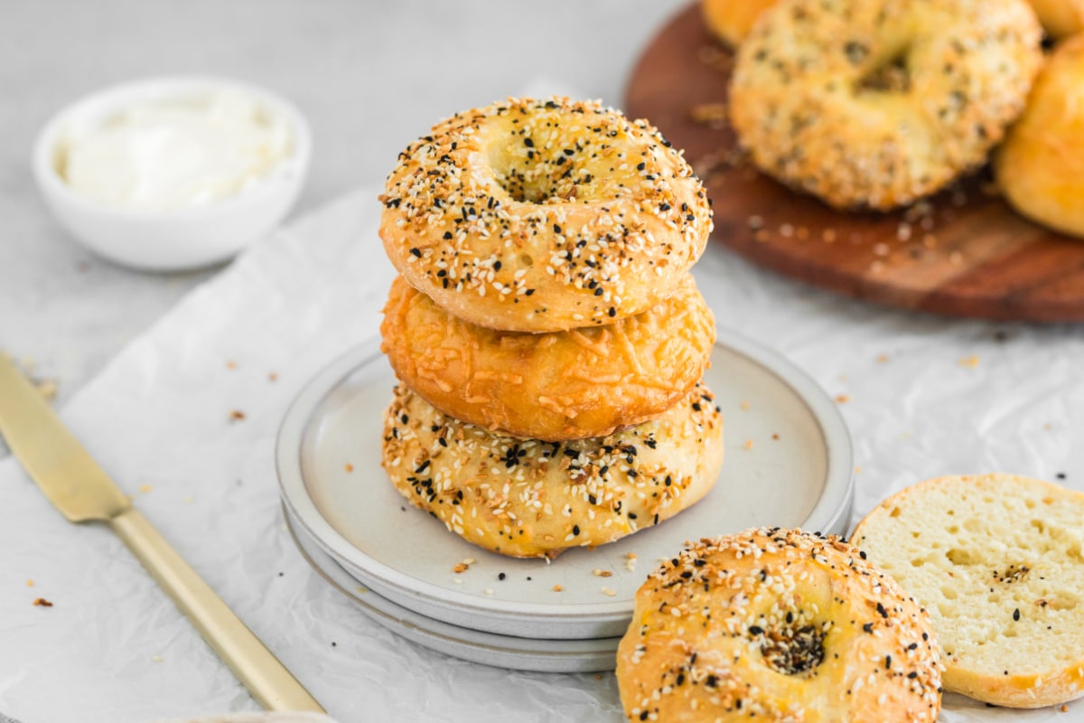 Three 3 ingredient bagels stacked on a white plate next to a dish of cream cheese.
