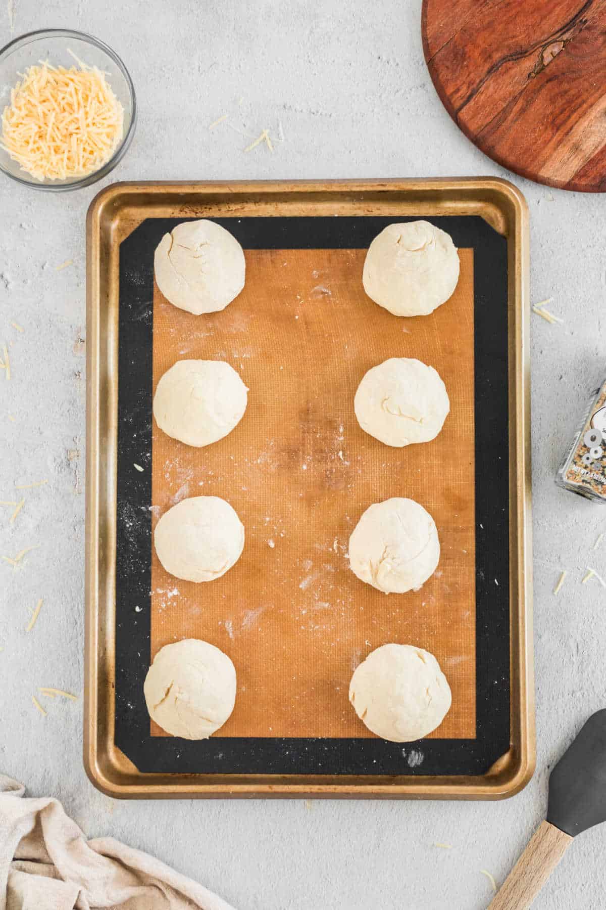 Eight balls of bagel dough on a baking sheet. 