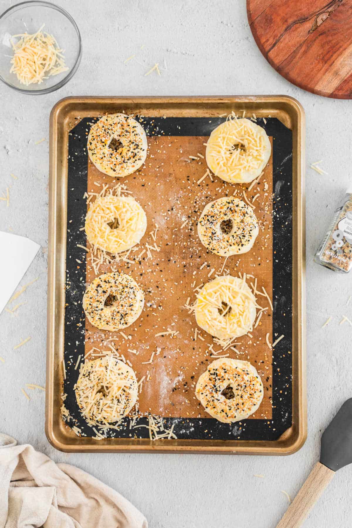 Bagel dough topped with toppings like shredded cheese and poppy seeds. 