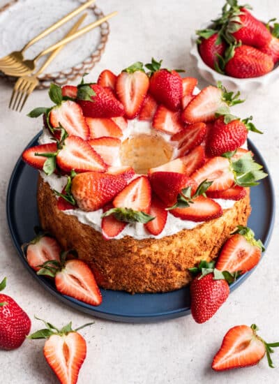 A homemade angel food cake topped with whipped cream and sliced strawberries on a blue platter.