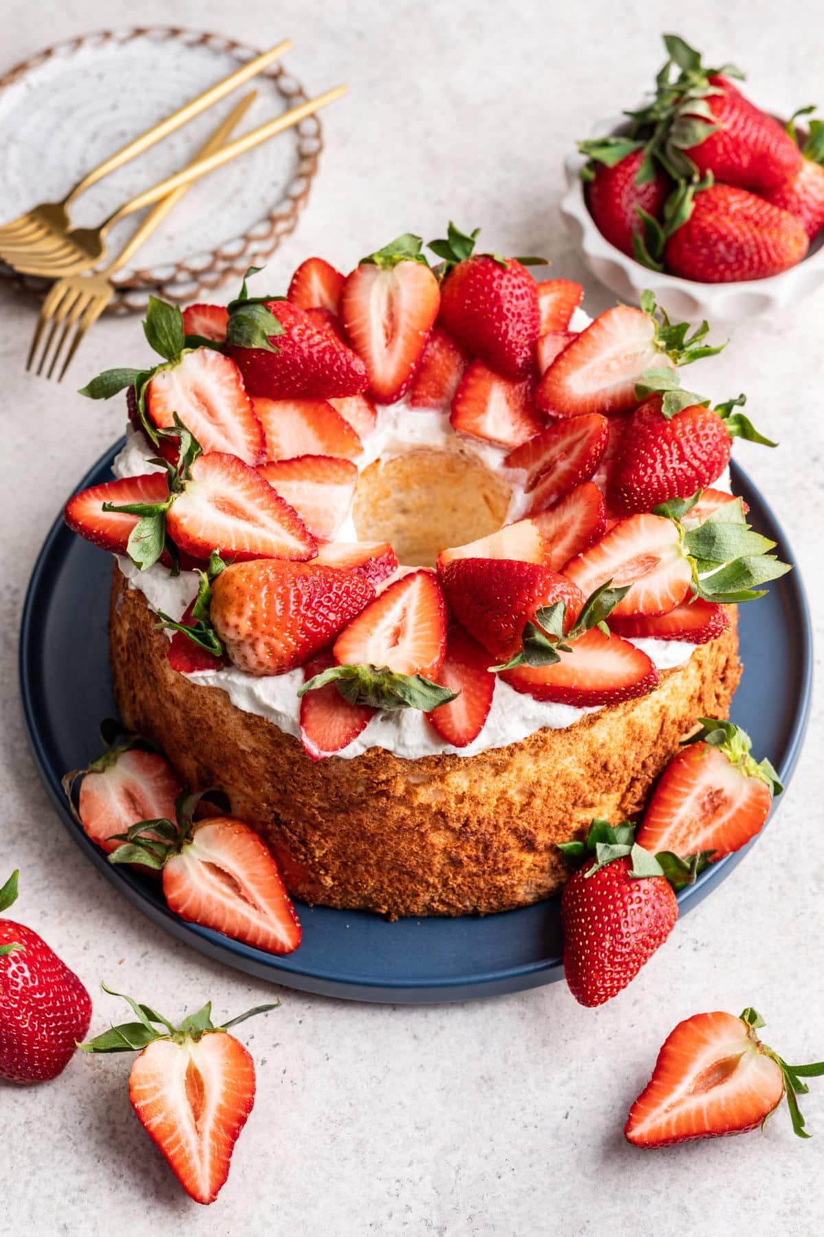 A homemade angel food cake topped with whipped cream and sliced strawberries on a blue platter.