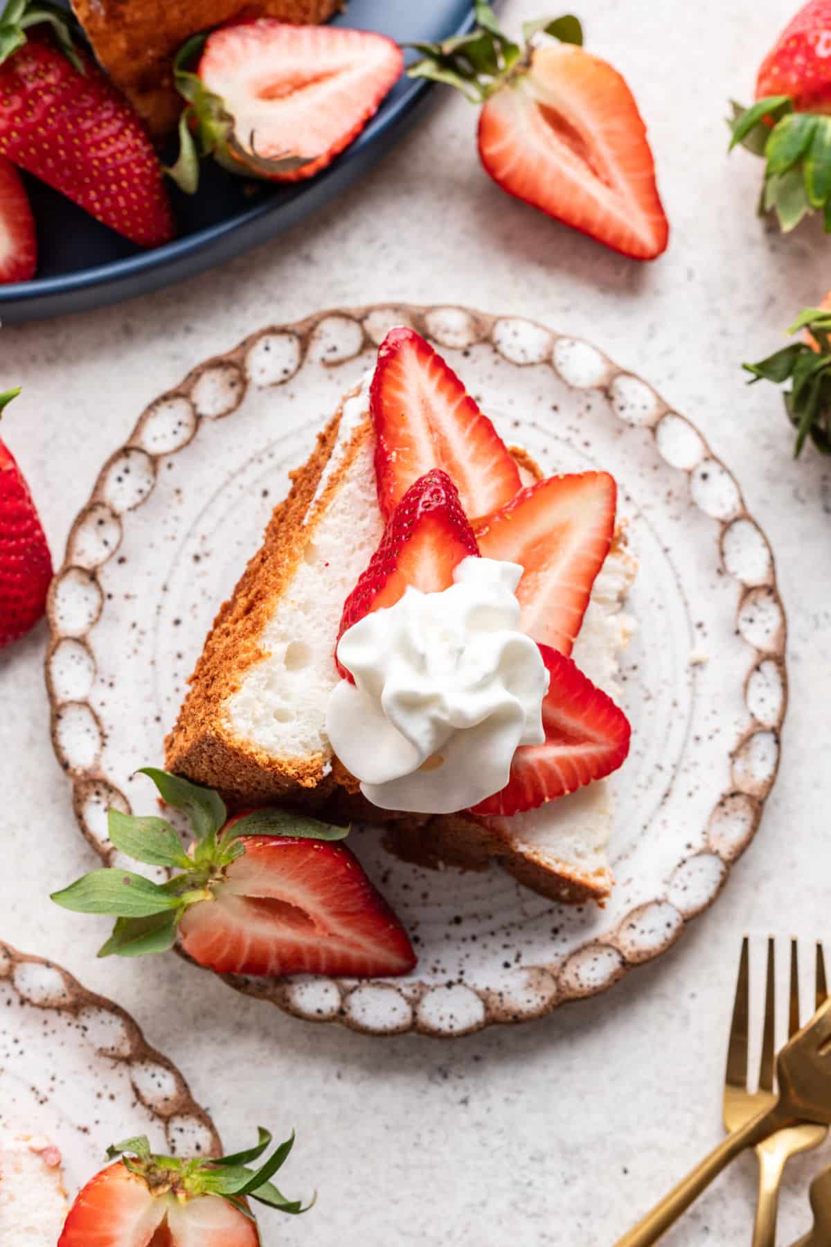A plate with a slice of angel food cake topped with sliced strawberries and whipped cream.
