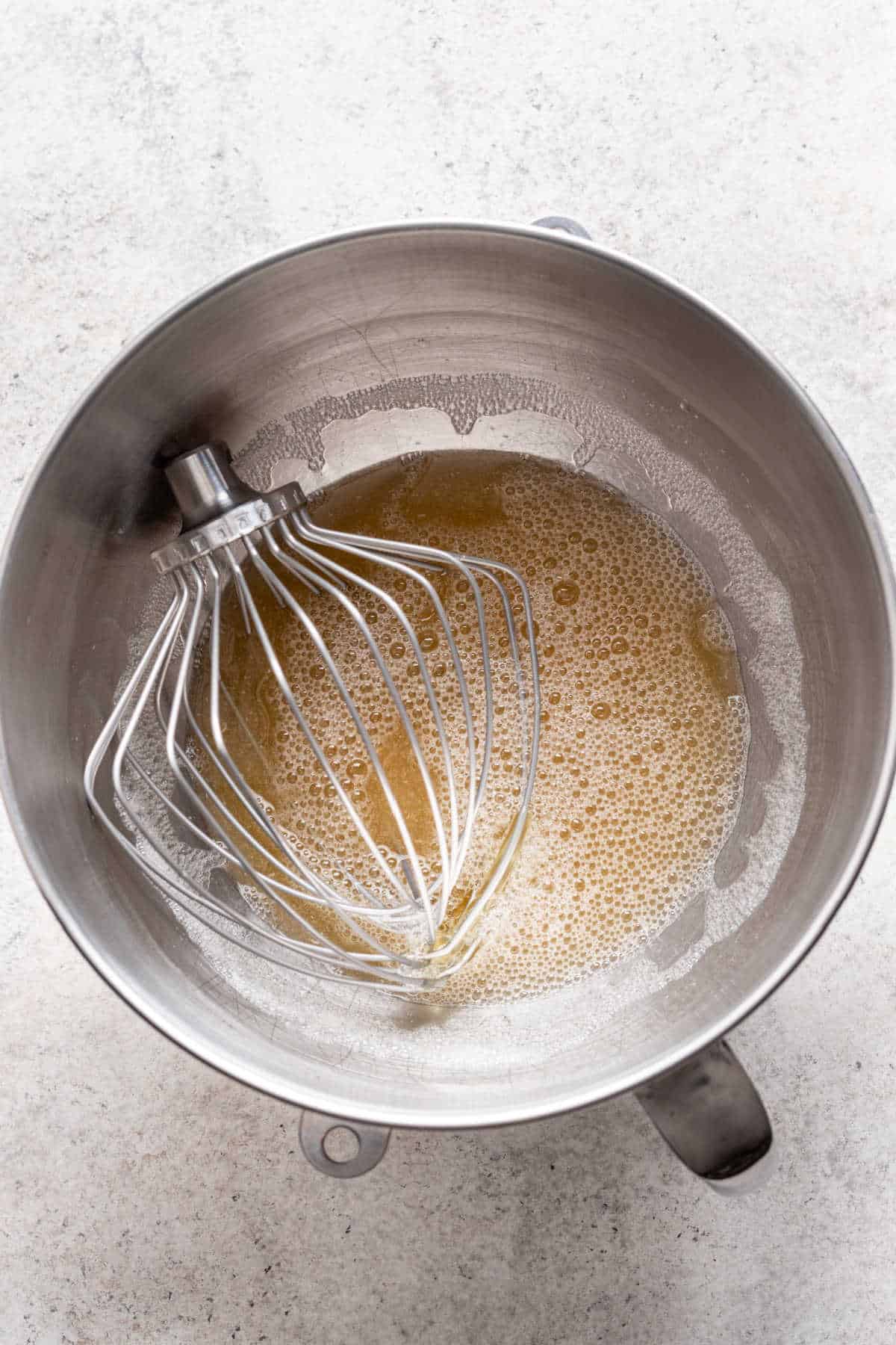 A whisk attachment in a bowl with egg whites water and vanilla.