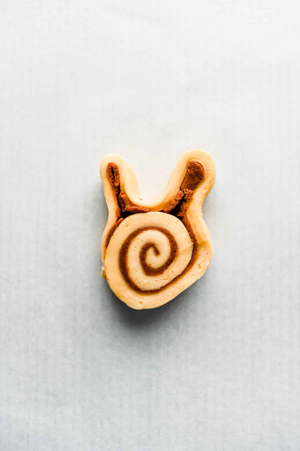 A bunny cinnamon roll on a parchment lined baking sheet. 