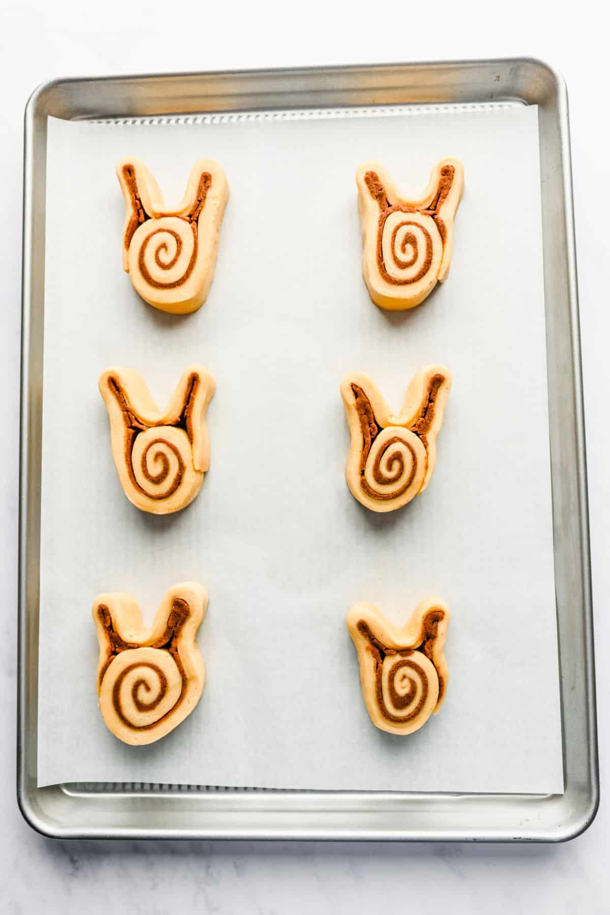 Unrisen bunny cinnamon rolls on a baking sheet. 