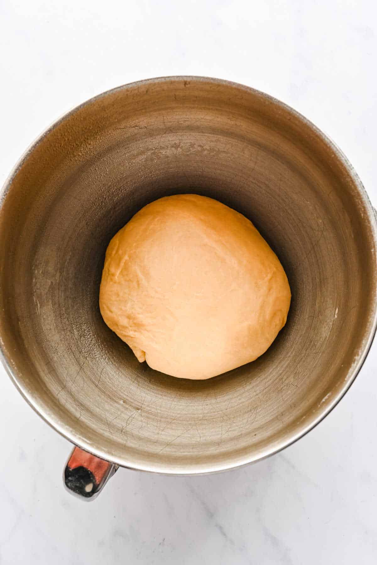 Unrisen cinnamon roll dough in a silver mixing bowl. 