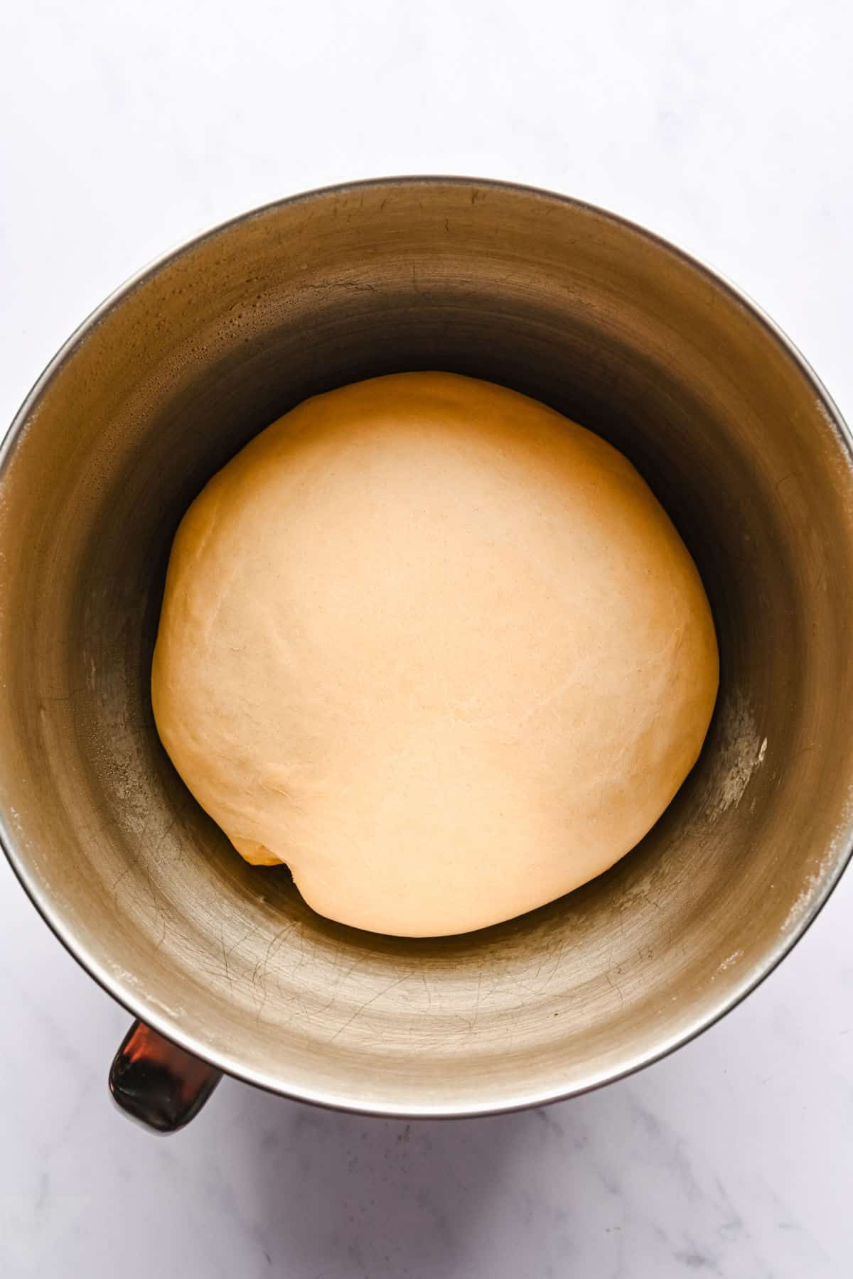 Risen cinnamon roll dough in a silver mixing bowl. 