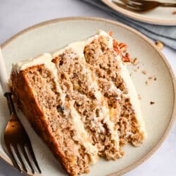 A slice of hummingbird cake on a cream plate with a fork.