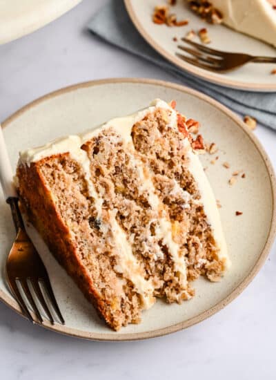 A slice of hummingbird cake on a cream plate with a fork.
