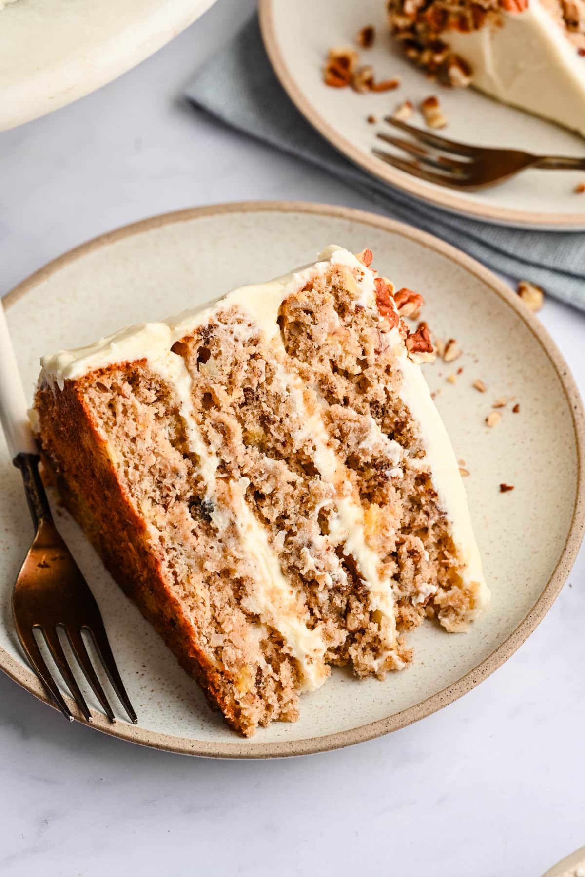 A slice of hummingbird cake on a cream plate with a fork.