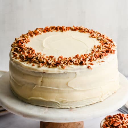 Hummingbird cake topped with chopped pecans on a marble cake stand.