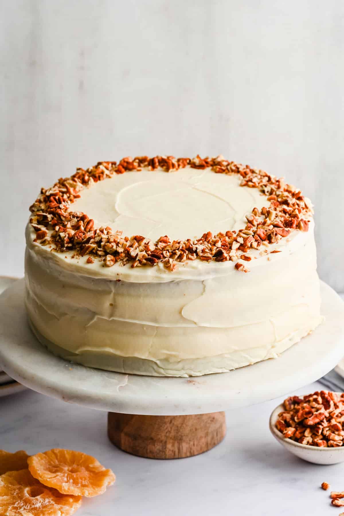 Hummingbird cake topped with chopped pecans on a marble cake stand.