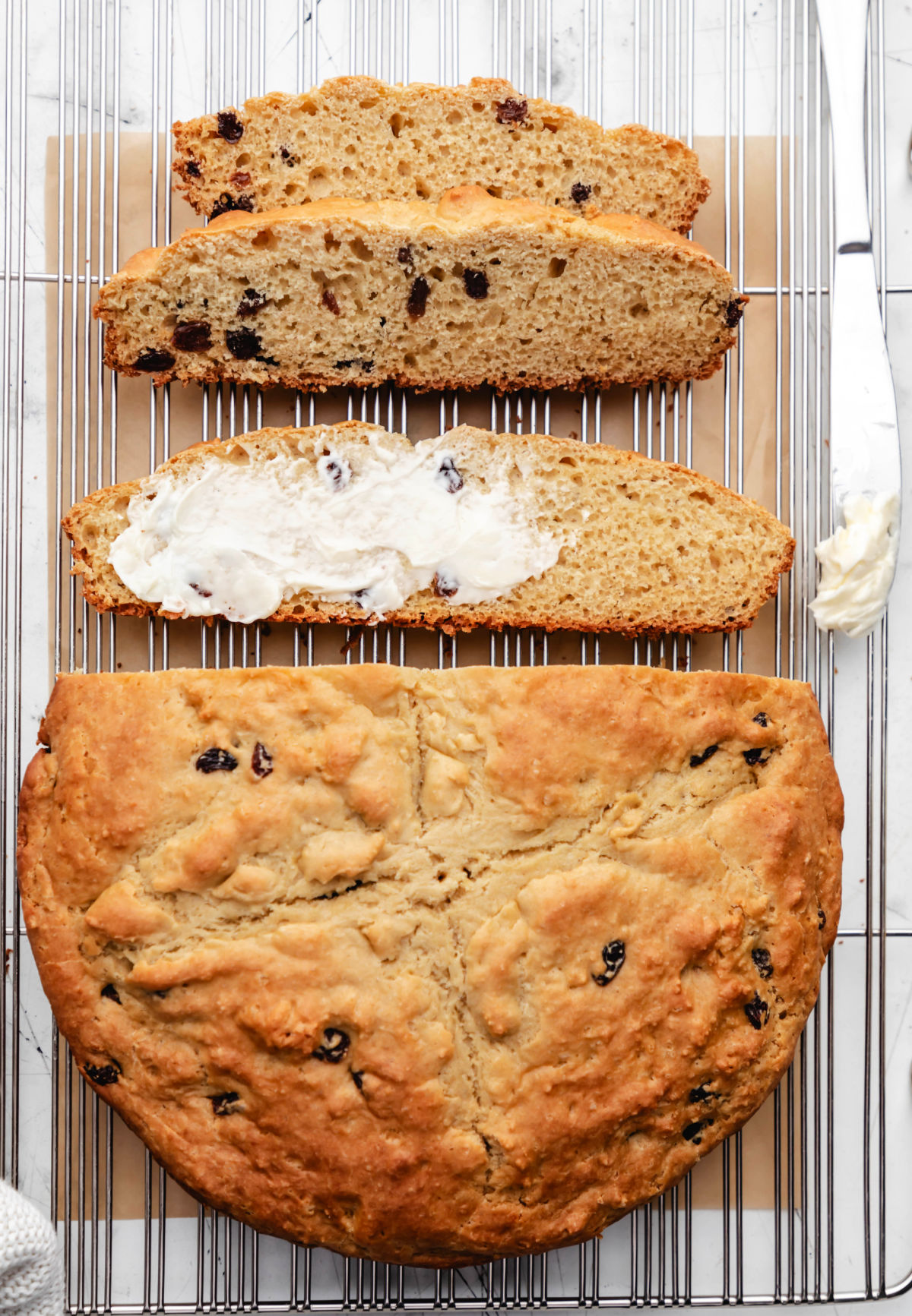 A half-buttered slice of Irish soda bread next to a sliced loaf of bread.