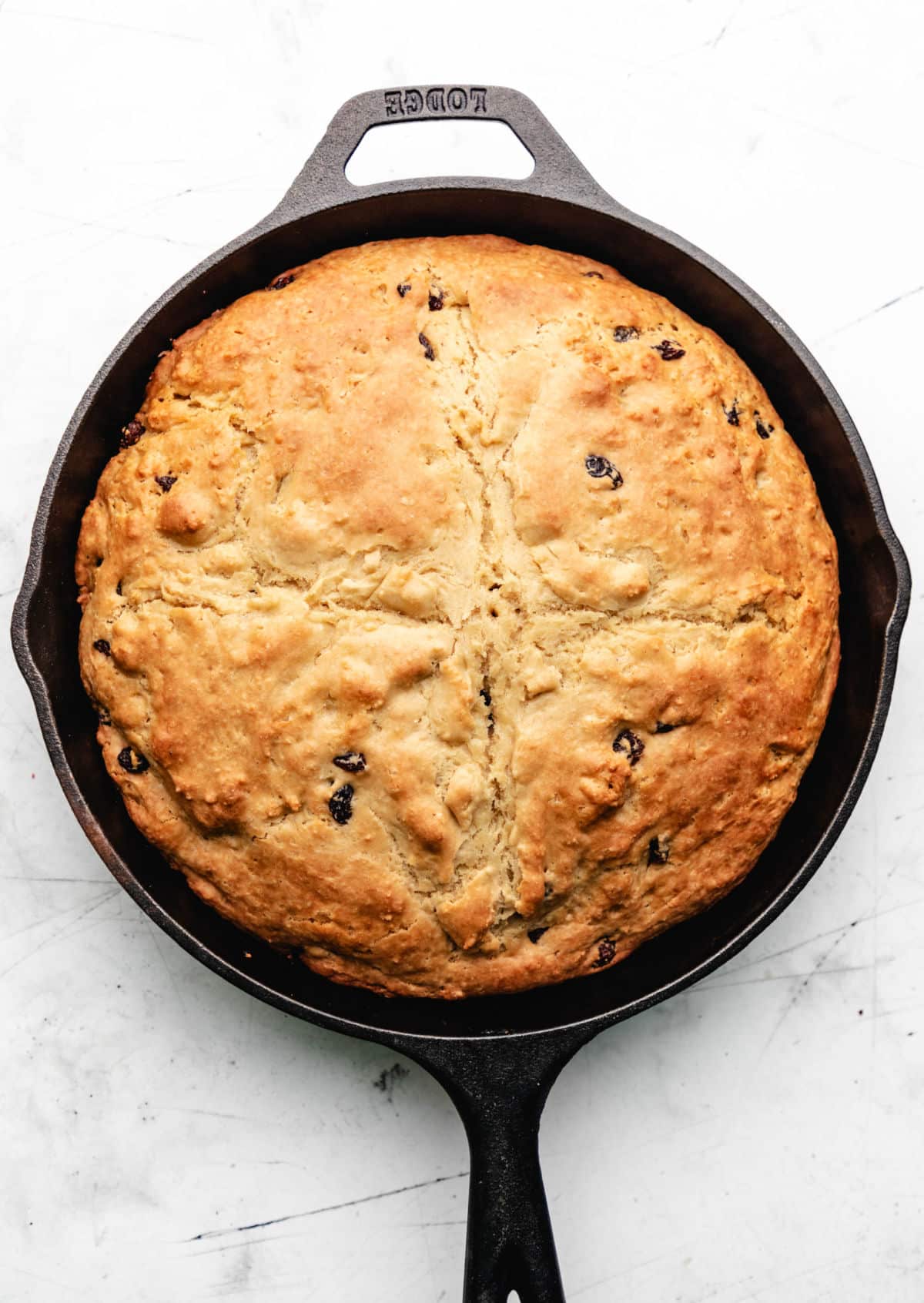 A baked loaf of Irish soda bread in a cast iron skillet. 