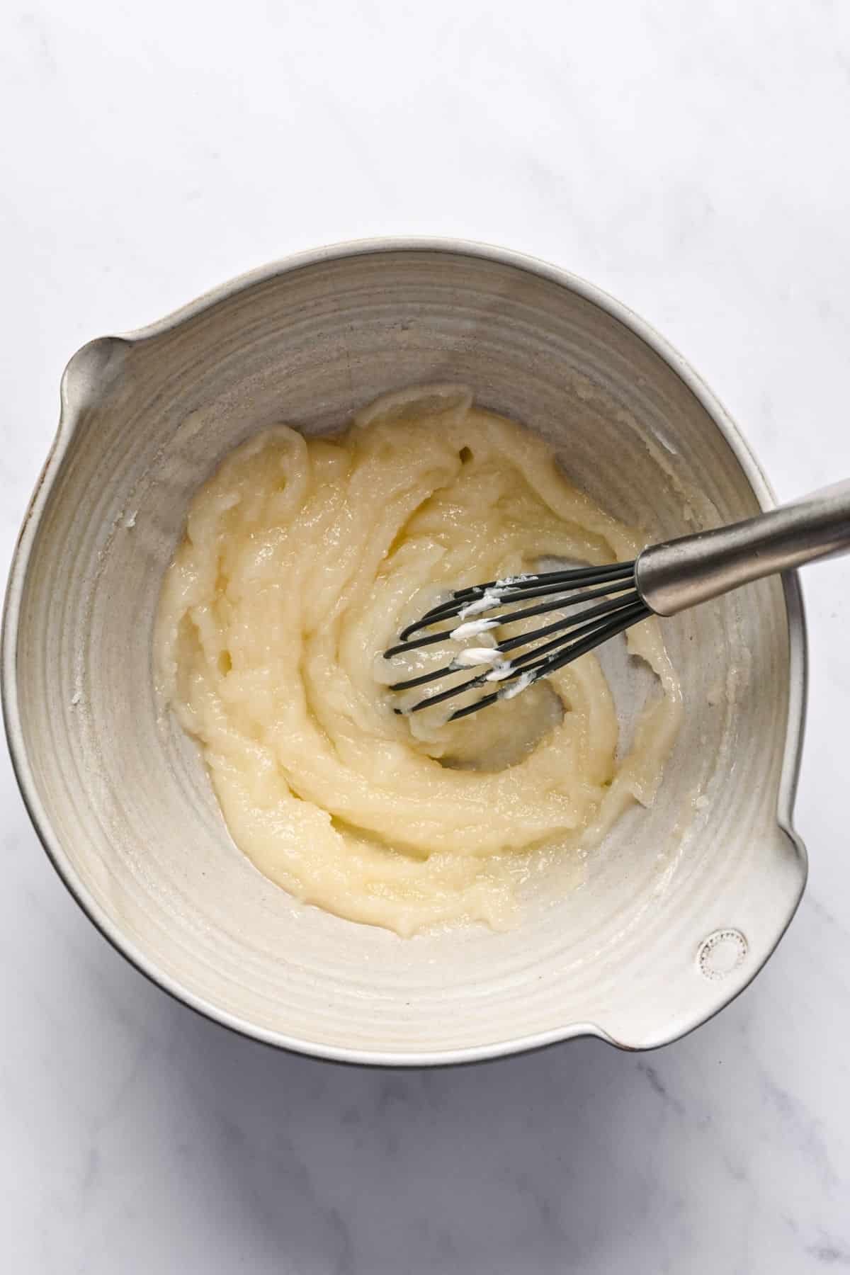Icing for lemon loaf cake in a mixing bowl with a whisk in it.
