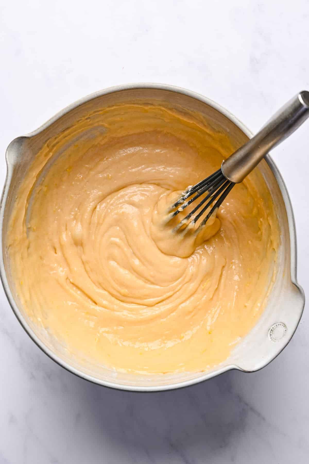 Lemon loaf cake batter in a mixing bowl with a whisk in it. 