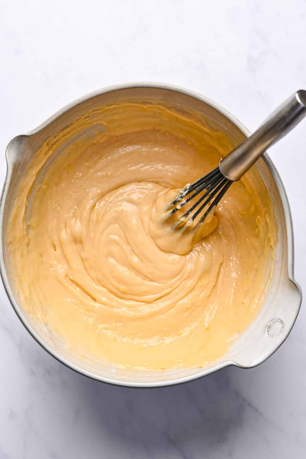 Lemon loaf cake batter in a mixing bowl with a whisk in it.