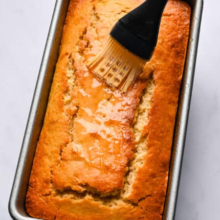 A basting brush brushing lemon syrup on top of lemon loaf cake.