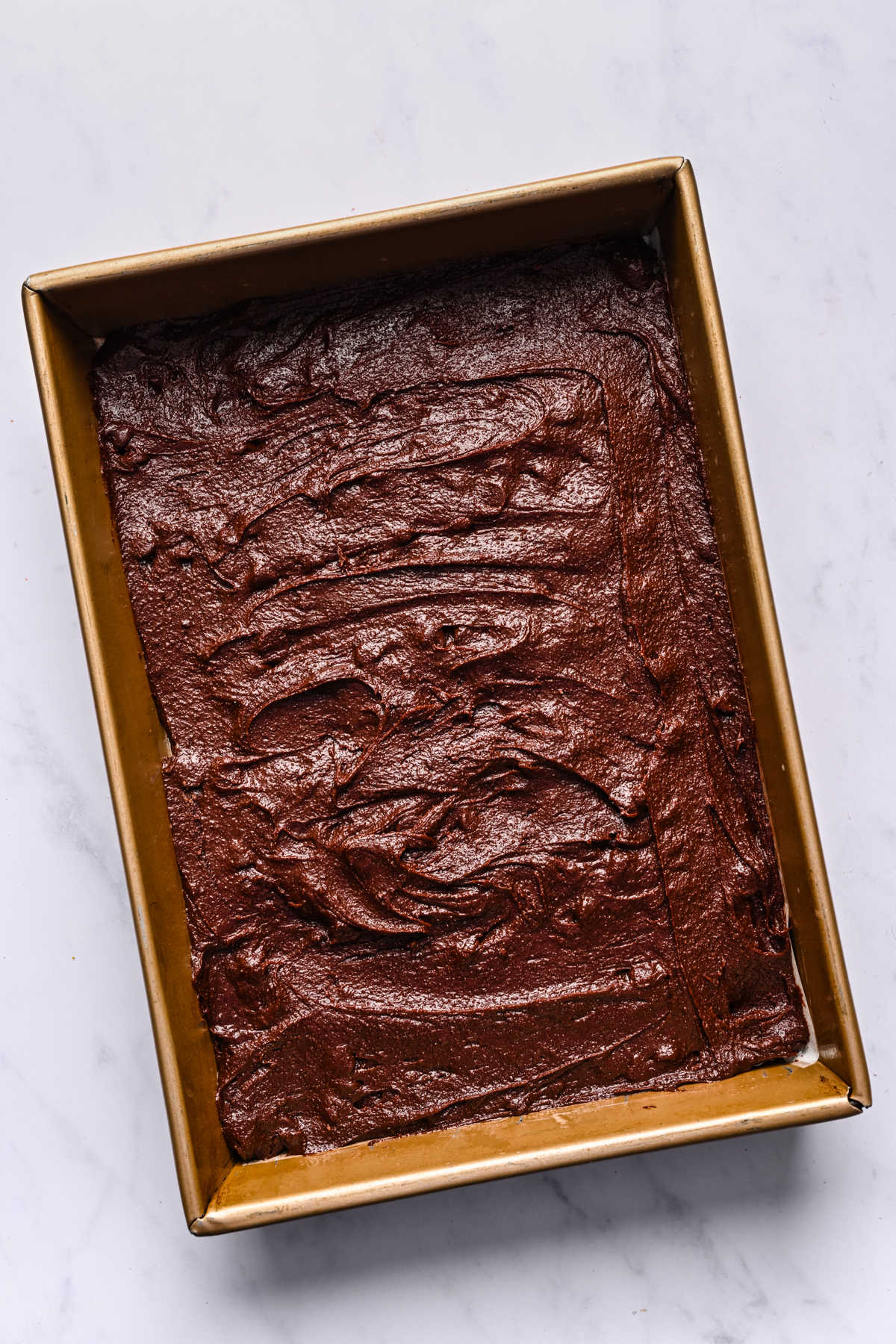 Brownie batter spread in a metal baking pan.