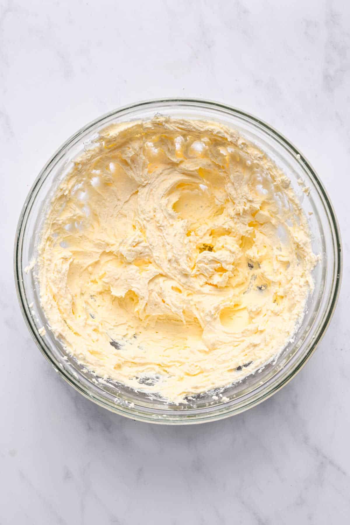 Beaten cream cheese in a glass mixing bowl. 
