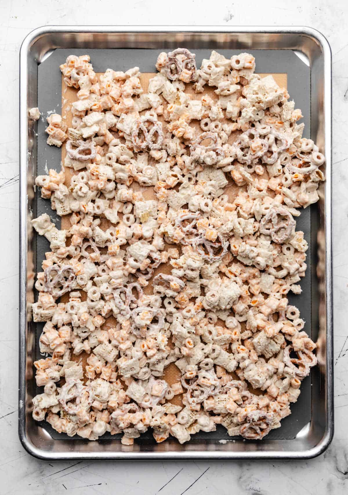 Almond bark coated cereal and pretzels on a baking sheet.