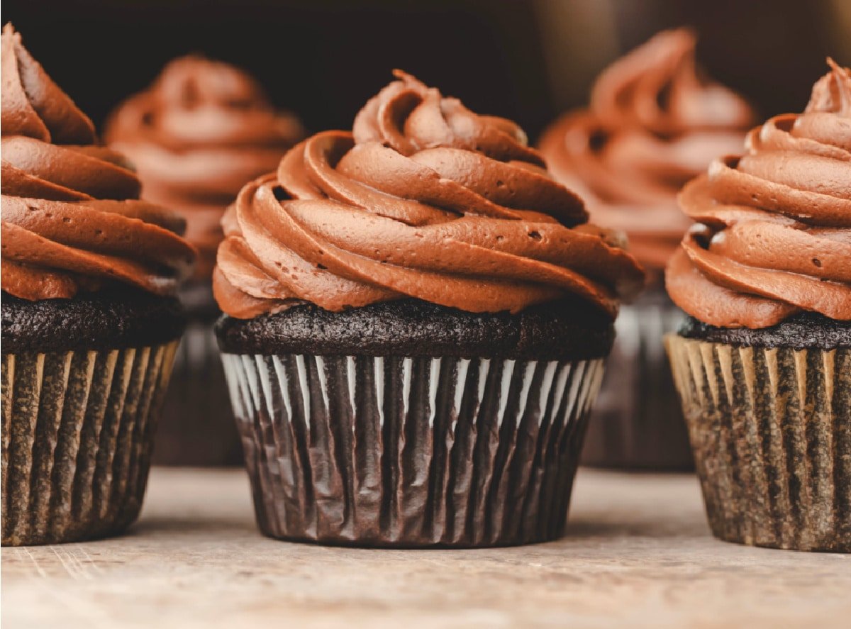 Three chocolate cupcakes topped with chocolate frosting in a row.