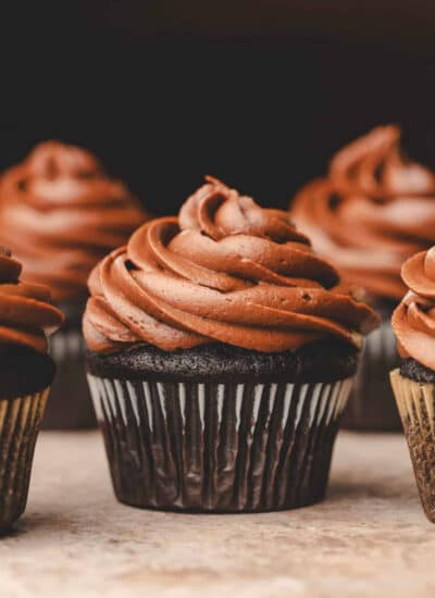 A chocolate cupcake topped with chocolate frosting surrounded by other cupcakes.