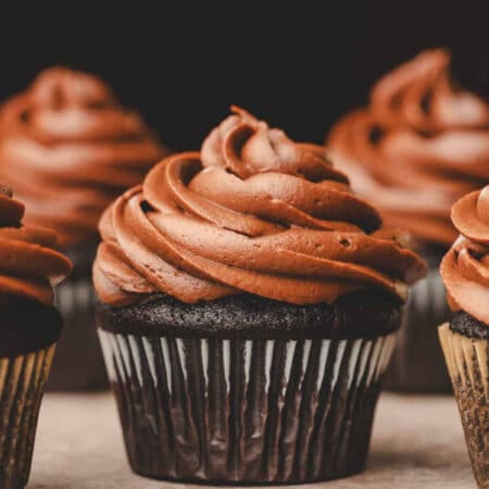 A chocolate cupcake topped with chocolate frosting surrounded by other cupcakes.