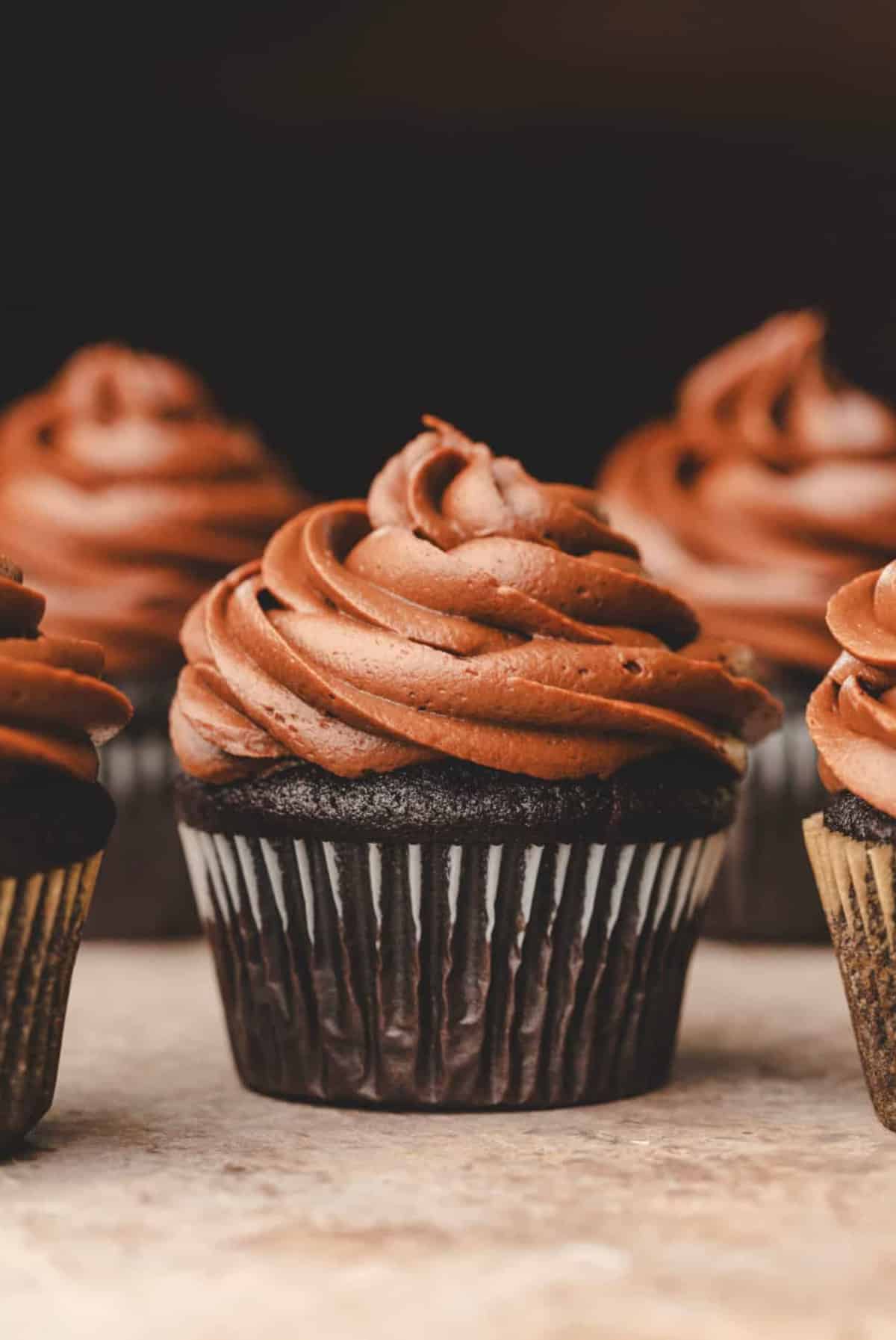 A chocolate cupcake topped with chocolate frosting surrounded by other cupcakes.